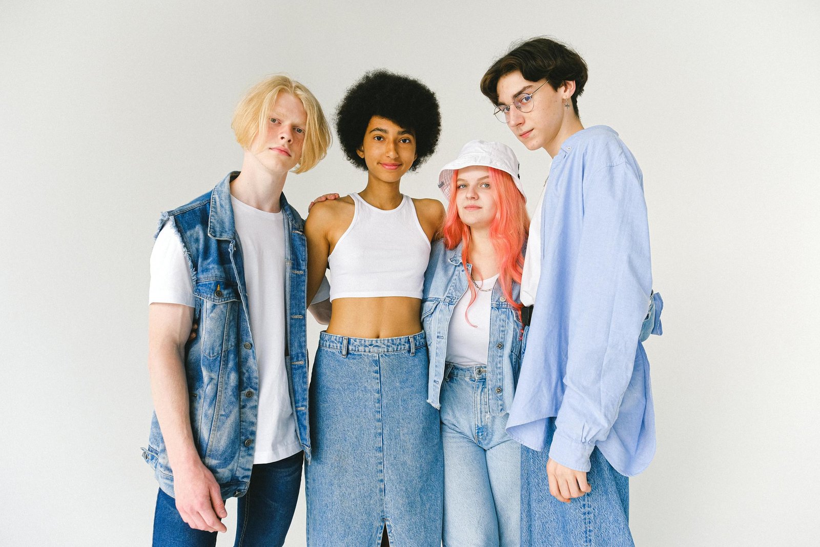 Content diverse teenager friends wearing denim clothes standing against white background hugging and looking at camera